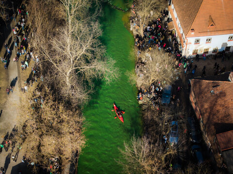 Aerial view of a vibrant river reflecting the sky, as crowds gather along the banks near St. Patrick's Day, Vilnius, Lithuania.
