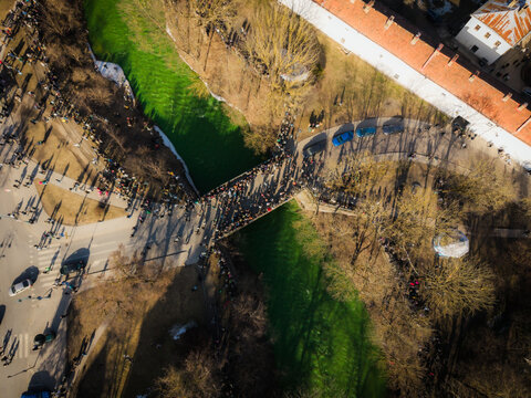 Aerial view of the vibrant green river snaking past the bustling crowds celebrating St. Patrick's Day near the Bernardine Garden, Vilnius, Lithuania.