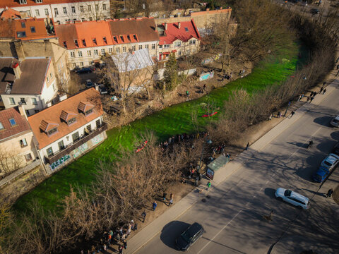 Aerial view of a vibrant green river dyed for St. Patrick's Day winds through the city's heart, contrasting with the aged buildings, Vilnius, Lithuania.