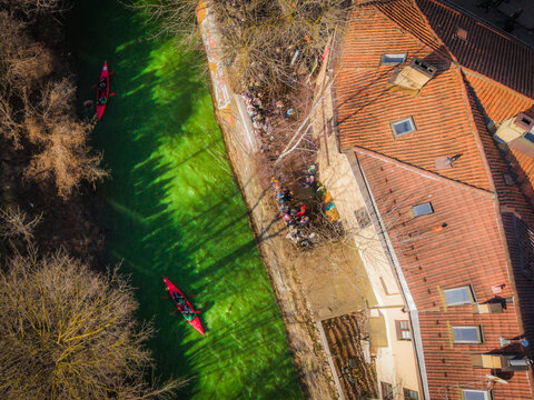 Aerial view of the vibrant green river snaking past the red-tiled roofs and bare trees, a celebration of St. Patrick's Day in full swing, Vilnius, Lithuania.