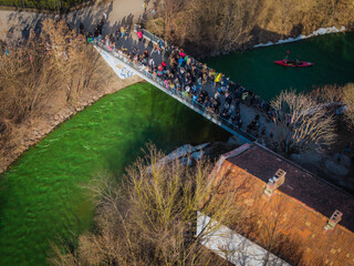 Aerial view of a vibrant crowd crossing a bridge over the river, the scene awash in the green hues of St. Patrick's Day celebrations, Vilnius, Lithuania.