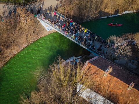 Aerial view of a vibrant crowd crossing a bridge over the river, the scene awash in the green hues of St. Patrick's Day celebrations, Vilnius, Lithuania.