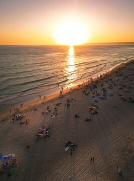 Aerial view of golden sunlight paints the beach, casting long shadows as people gather along the shore, Vejer de la Frontera, Andalusia, Spain.