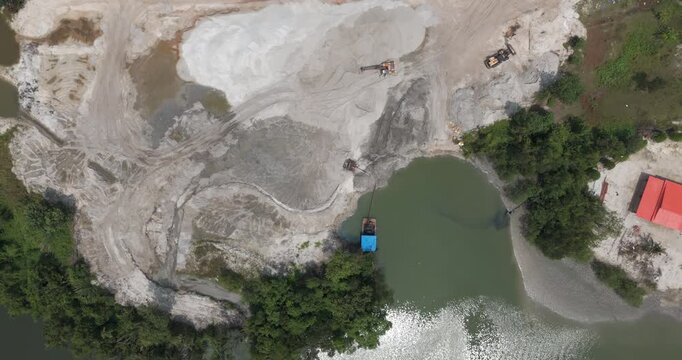 Aerial turning top down view of a sand dredging operation featuring a pump barge, excavators, and lush forest.