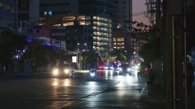 Urban metropolis street with cars and motorcycles driving at night in Bangkok, Thailand with illuminated skyscraper background