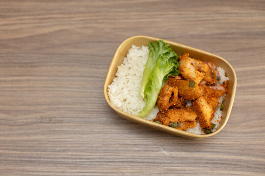 Fried pork larb with rice is placed in a box on the wooden floor, leaving space for copying.