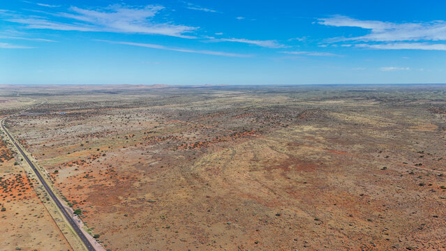 Aerial view of sun-baked earth stretches to the horizon, bisected by a lonely road under the vast blue sky, Karoo Desert, Northern Cape, South Africa.