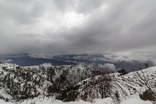 Aerial view of snow-dusted peaks pierce through the mist, a tranquil scene painted in shades of white and gray under a brooding sky, Pir Chanasi, Azad Kashmir, Pakistan.