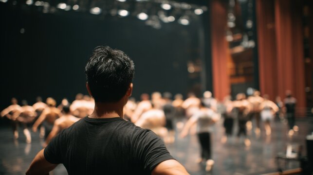 Seen from behind, a dance professional guides performers, with softly blurred dancers emphasizing direction, rhythm, and the creative flow of choreography.
