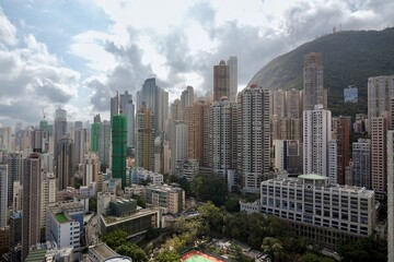 Obraz premium A sprawling view of high-rise apartment buildings and office towers nestled against the steep green hills of Hong Kong Island