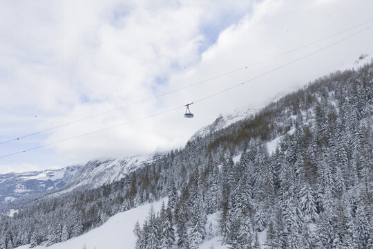 Aerial view of a lone cable car suspended high above snow-laden evergreen trees clinging to the steep slopes of Col du Pillon, Ormont-Dessus, Vaud, Switzerland.