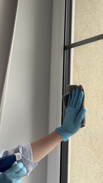 Hand of woman in blue rubber gloves cleaning the window with a rag and spray glass cleaner close up. Doing household chores, clean home concept, cleaner occupation, cleaning service, seasonal refresh