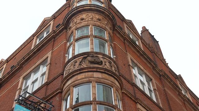 Red brick corner building in London viewed from a low angle showing curved windows and decorative facade details. Daytime view of residential architecture against the sky