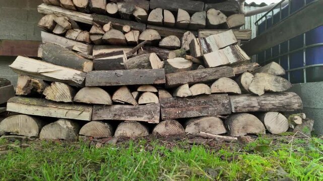 A tilt up shot revealing stacked firewood beside a rainwater tank, illustrating home heating and rising firewood cost.