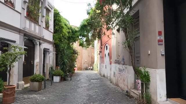 Peaceful narrow street lined with traditional architecture, lush green ivy, and cobblestone pavement in a historic Roman neighborhood. Authentic Italian urban landscape with character.