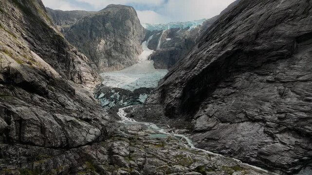 Glacier descending between steep mountain faces with glacial stream and ice, Norwegian wilderness.