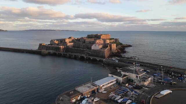 St Peter Port Harbour,Guernsey,low forward flight towards Castle Cornet in golden hour sun with Jethou and Sark beyond ,calm sea and interesting sky
