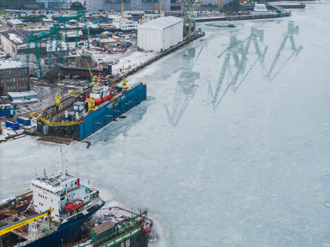Aerial view of ships docked in the icy waters, with reflections of cranes creating a stark contrast against the frozen harbor, Gdansk, Poland.