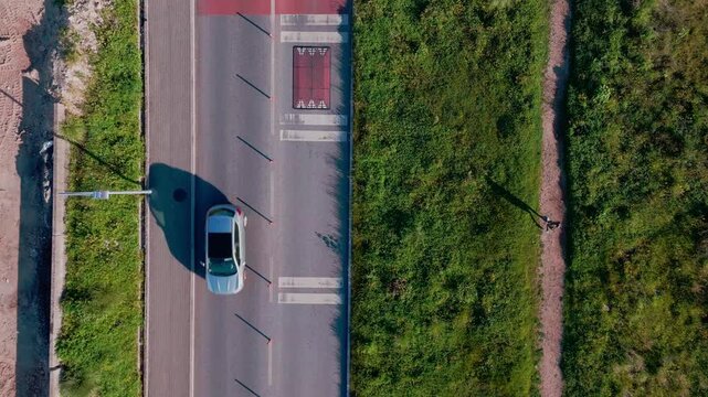 Top down drone shot showing cars moving on a road with a parallel dirt path where a person is walking in a rural landscape.