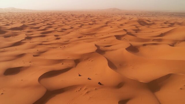 High altitude drone orbit over Morocco desert dunes with small vehicles