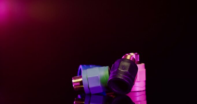 Close up of various colorful plastic industrial pipe fittings and threaded connectors against a dark background with red light
