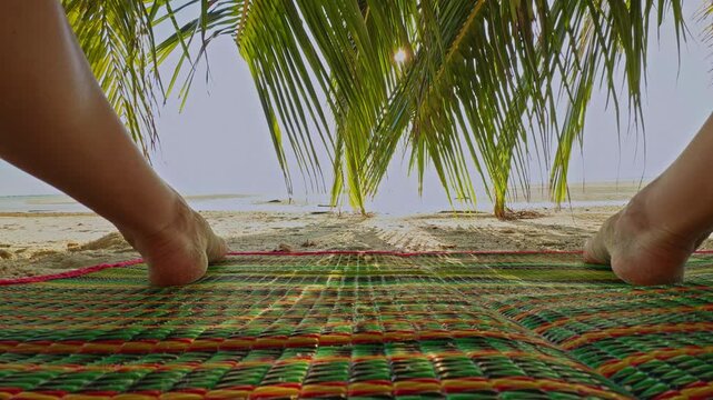 First Person View of Bare Feet Positioned Wide Apart on Colorful Mat Under Palm Leaves with Bright Sun and Calm Sea in Background, Low Angle Perspective Showing Relaxed Tropical Freedom and Open Space