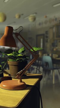 A teachers desk is shown with a lamp and a green plant. The setting is a classroom with chairs and educational posters in the background. Light fills the room through windows.