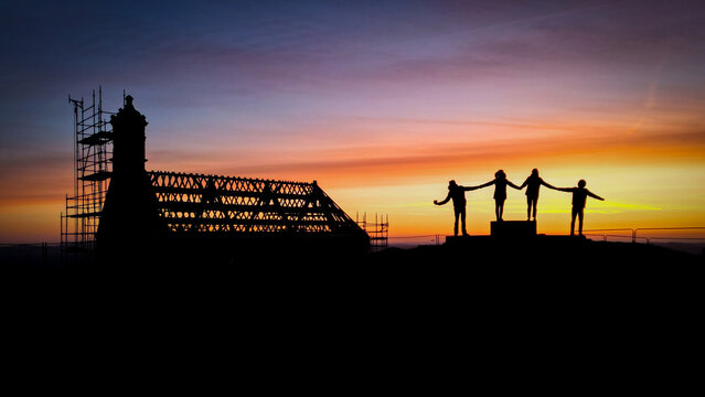 Aerial view of the Mont Saint Michel de Brasparts silhouetted against a vibrant sunrise, with figures atop, Saint-Rivoal, Bretagne, France.