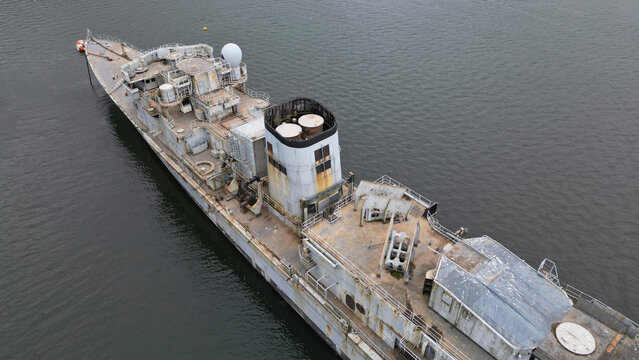 Aerial view of a weathered and decaying ship with visible rust and peeling paint contrasts against the dark water, Landevennec, France.