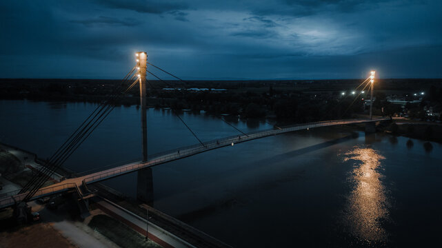 Aerial view of illuminated bridge reflecting in the still waters of the river under a darkening sky, Sremska Mitrovica, Vojvodina, Serbia.
