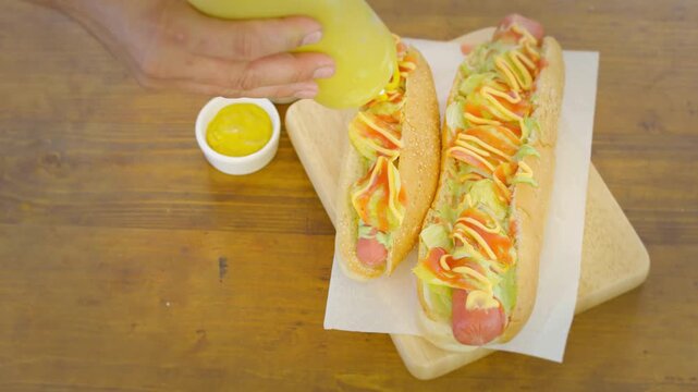 Two hot dogs on a wooden tray with condiments on a table