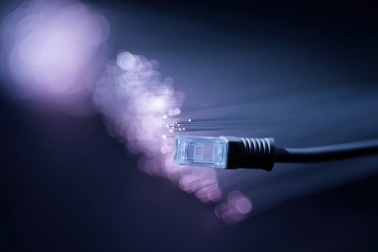 Close-up RJ45 ethernet cable connected to network port with illuminated fiber optic cables representing high speed data transfer