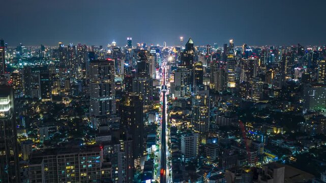 Bangkok downtown skyline illuminating cityscape with bustling highway traffic, urban skytrain, soaring skyscraper buildings at night from aerial