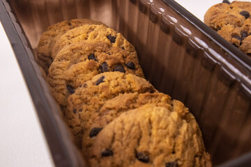 Fototapeta premium Delicious chocolate chip cookies arranged inside a dark plastic tray with a small stack on the side isolated on a white background.