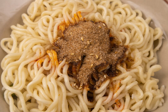 Macro close-up shot of cooked instant noodles topped with dry seasoning powder, salt, and spices, showing the detailed texture of the flavorings and wavy noodles.