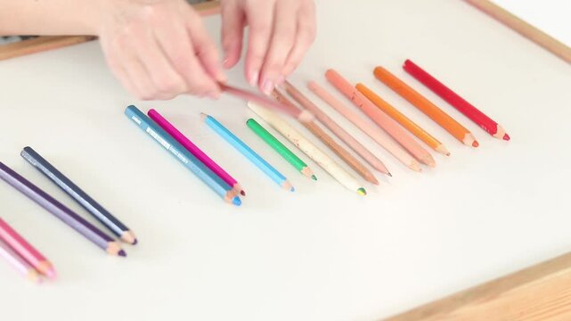 Hands sorting colored pencils by color gradient on white table, close-up