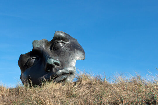 Maskenartiges Gesicht, die Bronzeskulptur &bdquo;Licht des Mondes&ldquo; (Light of the Moon) von Igor Mitoraj in den D&uuml;nen von Scheveningen in Den Haag, Niederlande.