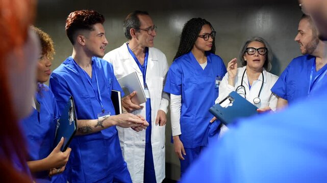 Diverse hospital team of doctors and nurses in scrubs chatting and laughing in a corridor during a break, friendly multiethnic colleagues fostering teamwork and positive workplace energy