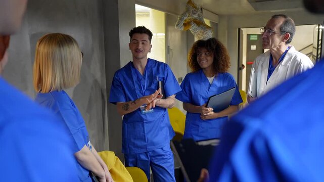 Multiethnic group of medical students and a senior doctor discussing a clinical case in a hospital hallway during a training lesson, highlighting healthcare education and teamwork