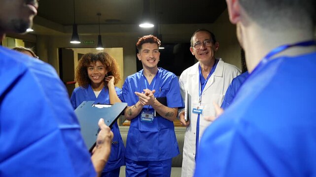 Diverse group of doctors and nurses wearing scrubs and lab coats having a positive and collaborative conversation during a meeting in the hospital corridor, showing teamwork and dedication