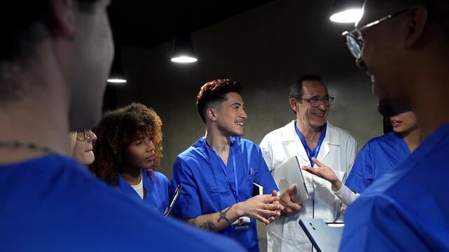 Senior male doctor mentoring a diverse group of young medical interns and nurses during a meeting, discussing patient cases and sharing knowledge in a modern clinic education session