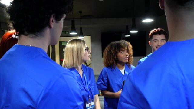Multiethnic team of young doctors and nurses in blue scrubs having a friendly conversation during a break, standing together in a modern clinic and sharing ideas for a medical case