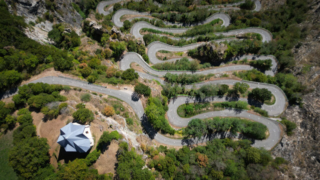 Aerial view of the winding road snaking through the rugged terrain, a ribbon of grey against the green, Montvernier, Auvergne-Rhone-Alpes, France.