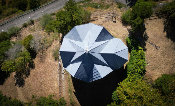Aerial view of a unique geometric building with a starburst roof pattern stands out amidst the dry grass and surrounding green trees, Montvernier, Auvergne-Rhone-Alpes, France.