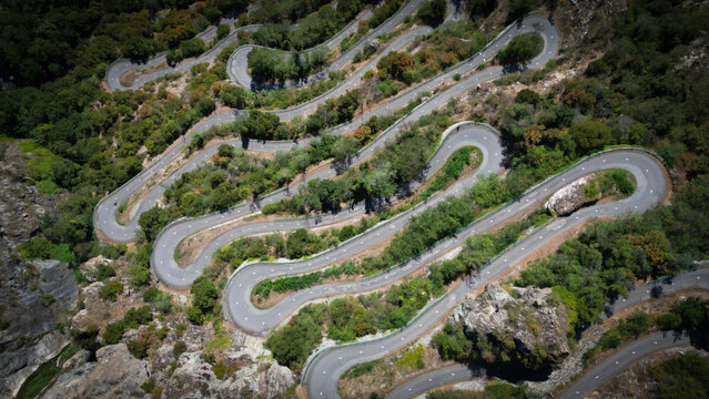Aerial view of a serpentine road winding through lush green hills, a testament to human engineering against the rugged landscape, Montvernier, Auvergne-Rhone-Alpes, France.
