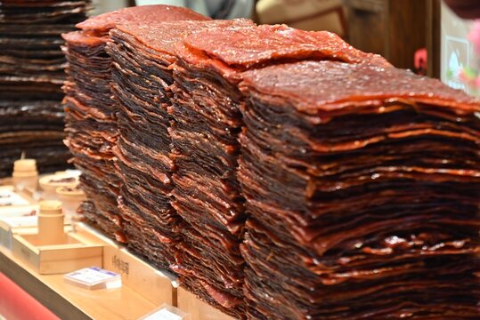 Stacks of glossy beef jerky displayed at a food market, showcasing traditional savory snack products ready for sale.