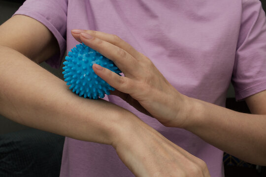 Woman uses blue spiky massage ball on forearm, self massage routine for muscle tension relief