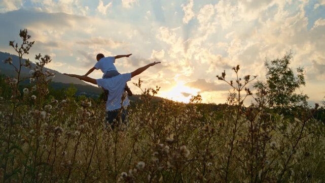 Father carries small boy on shoulders in field at sunset. Physical contact and shared activities build strong family foundations and support healthy emotional growth in kids