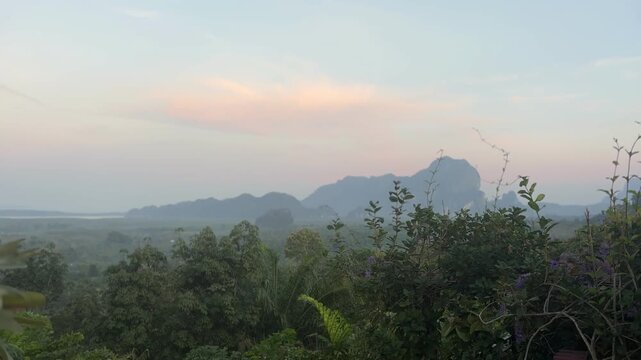 Soft sunrise sky above forest and distant limestone hills at Din Daeng Doi in Krabi Thailand with gentle colors, light haze, and calm tropical landscape scenery