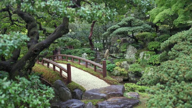 Wooden bridge crossing a tranquil Japanese garden with stones and pruned trees in Kyoto Japan peaceful travel destination
